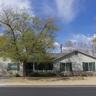 A single-story house with a tree in front, situated along a street under a blue sky with clouds.