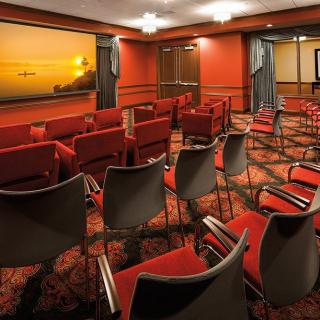 A conference room with neatly arranged chairs facing a large window, offering a sunset view.