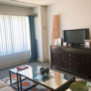 A cozy living room with a television, coffee table, and large window with curtains.