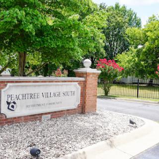 Entrance sign of Peachtree Village, surrounded by lush greenery.