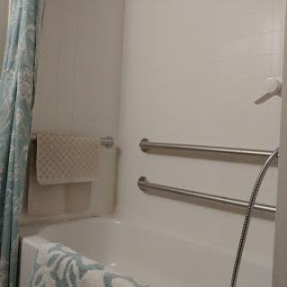 A tidy bathroom featuring a shower tub combination with grab bars for safety.