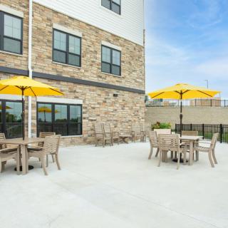 An outdoor patio area with wooden tables and chairs, featuring bright yellow umbrellas against a stone building facade.