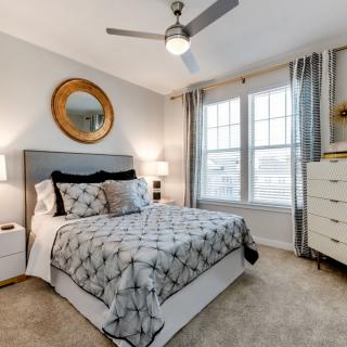 A modern bedroom with a double bed, decorative mirror, ceiling fan, and stylish furnishings.
