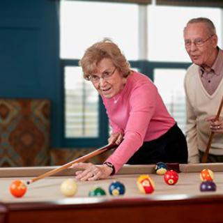 Two seniors enjoying a game of billiards together.