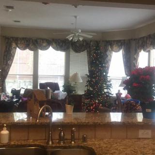 A cozy kitchen and living room setup with holiday decorations, including a Christmas tree near large windows with curtains.