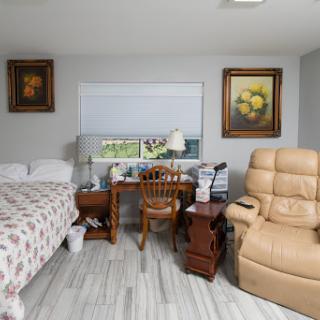 A cozy and well-furnished bedroom featuring a bed, desk, armchair, and decorative paintings.