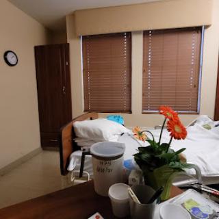 A view of a hospital patient room featuring a bed, medical supplies, and bright window blinds.