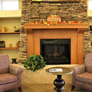 A cozy living room setting featuring a stone fireplace, comfortable armchairs, and autumn-themed dcor.