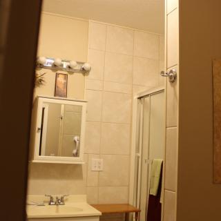 A view of a bathroom featuring a sink, mirror, and shower area with towels hanging.