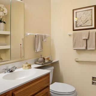 A well-organized bathroom with a sink, toilet, mirror, and neatly arranged towels.