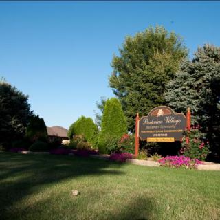 A tranquil outdoor scene featuring a landscaped area with a sign, surrounded by trees and blooming flowers.