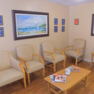 A cozy waiting room with chairs arranged around a small table, decorated with paintings and stocked with magazines.