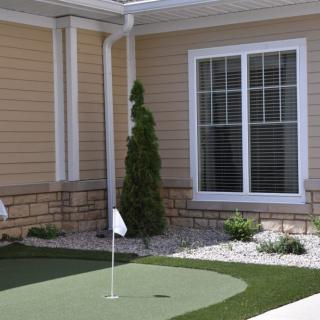 A backyard putting green next to a house with landscaped surroundings.