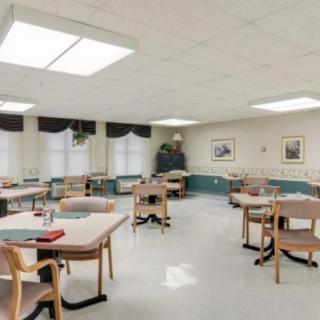 An empty dining room in a nursing home, featuring several tables and chairs.