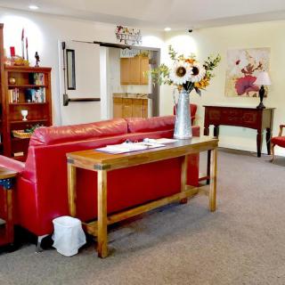 A cozy living room with a red couch, wooden furniture, decorative flowers, and artwork on the walls.