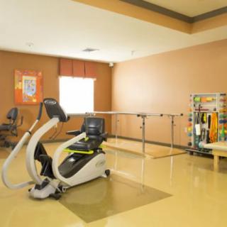 A rehabilitation room with exercise equipment, including a stationary bike and parallel bars.