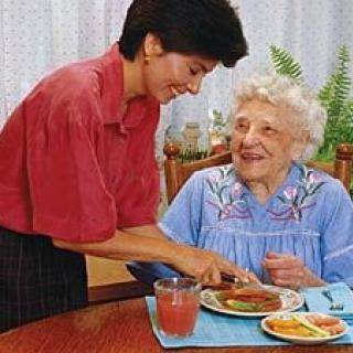 A caregiver assists an elderly woman during mealtime, as they share a moment of joy.