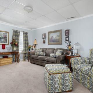 A cozy living room with patterned furniture, artwork on the walls, and a carpeted floor.