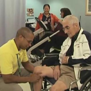 A physical therapist assists an elderly man with rehabilitation exercises in a healthcare setting.