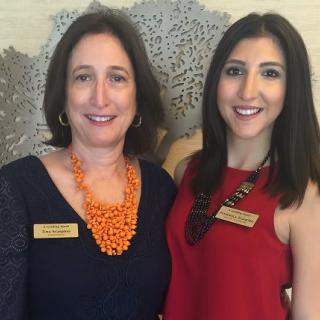Two women smiling indoors, wearing formal attire.