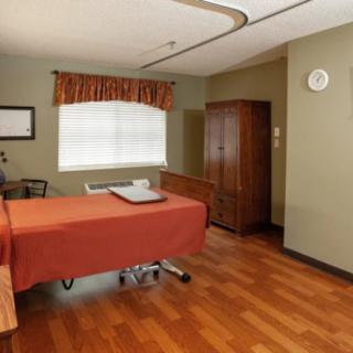 A well-maintained hospital room with a bed, wooden furniture, and a window with curtains.