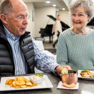 An elderly couple enjoys a meal and conversation in a cozy indoor setting.