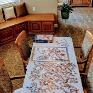 A cozy indoor setting with a puzzle in progress on the table, surrounded by chairs and a window seat.