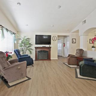 A cozy living room with multiple recliners, a television above a fireplace, and indoor plants enhancing the decor.
