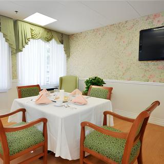 A cozy dining room with a neatly set table surrounded by four chairs and a television mounted on the wall.