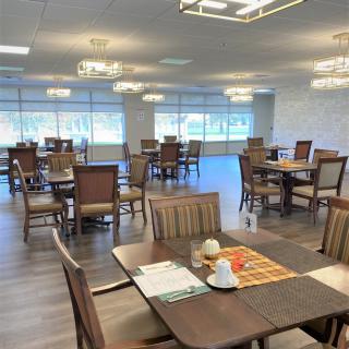 A spacious dining room with multiple tables and chairs, featuring elegant lighting and large windows.