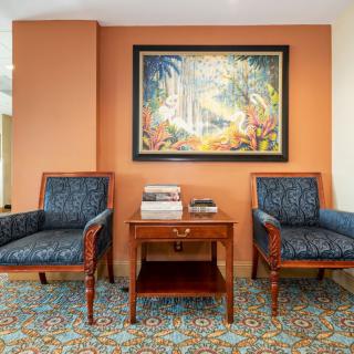 A cozy seating area with two chairs and a side table, featuring a vibrant painting and several books.