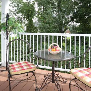 A cozy patio with a small table and two chairs, adorned with a basket of fruit and overlooking lush greenery.