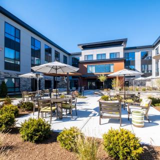 A modern building with a courtyard featuring outdoor seating and umbrellas.