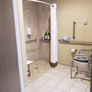 A spacious and accessible bathroom featuring a shower, wheelchair-friendly commode, and safety handrails.