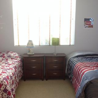 A bright bedroom with two twin beds, a shared dresser, and decorative items by the window.