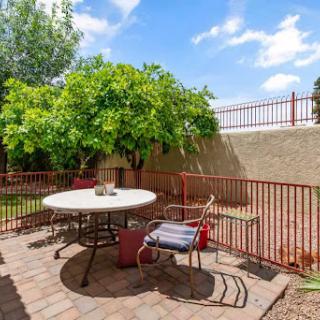 A serene outdoor patio area featuring a round table, chairs, and lush greenery under a clear blue sky.