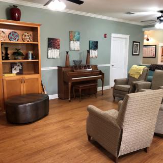 A cozy living room with comfortable chairs, a piano, and a bookshelf on a wooden floor.