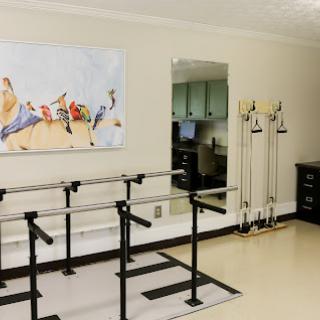 A rehabilitation therapy room featuring a ballet bar, exercise equipment, and a serene artwork.