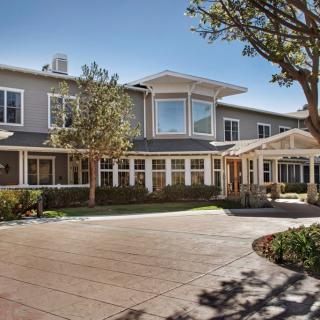 A large residential building with a driveway and trees on a sunny day.