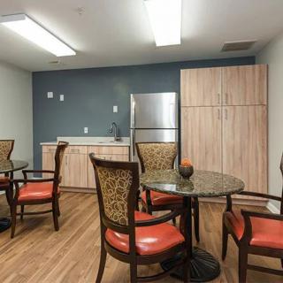 A cozy kitchen area with round tables, cushioned chairs, and modern appliances.