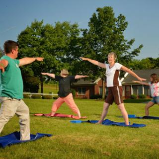 A group of children and adults practicing yoga together in a sunny outdoor setting.