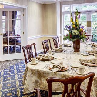 An elegant dining room with a table set for a meal, featuring a floral centerpiece and classic wooden chairs.