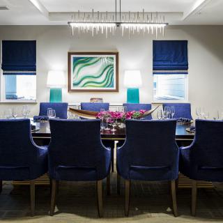 A modern dining room with blue chairs, a stylish chandelier, and contemporary artwork on the wall.