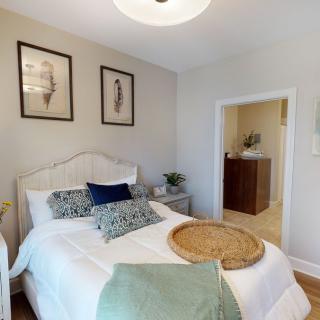 A cozy bedroom featuring a neatly made bed with decorative pillows, framed artwork on the wall, and natural light filling the space.