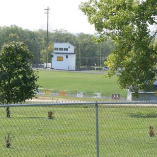 A view of a football field surrounded by trees and a chain-link fence.