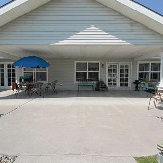 A spacious outdoor patio area with tables, chairs, and a blue umbrella in front of a house.