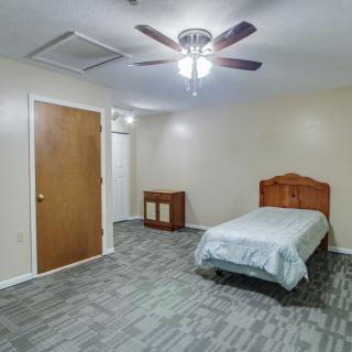A minimalist bedroom with a single bed, carpeted floor, and wooden furniture.