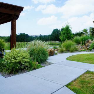 A serene garden with a winding concrete pathway surrounded by lush greenery and plants.