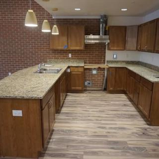 A modern kitchen featuring wooden cabinets, granite countertops, and a brick accent wall with pendant lighting.