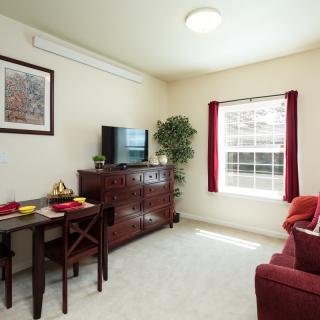 A cozy living room with a red theme, featuring a TV, dining area, and a large window.